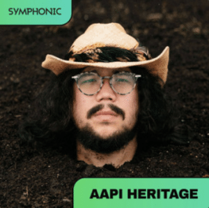 A person wearing glasses and a straw hat is partially buried in soil up to their neck. The image is labeled "SYMPHONIC" and "AAPI HERITAGE," suggesting a playlist celebrating diverse cultural roots.